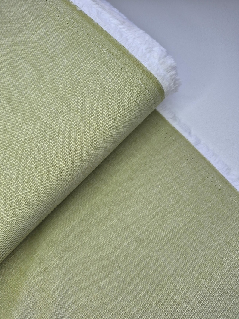 Puede incluir: Un rollo de tela verde claro con una superficie texturizada. La tela est&aacute; doblada, revelando un borde blanco con flecos. El material parece ser lino o un textil tejido similar, adecuado para proyectos de ropa o decoraci&oacute;n del hogar.