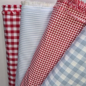 May include: Four rolls of fabric in various patterns. The fabrics include red and white gingham, light blue and white stripes, and red and white gingham. The edges of the fabric are frayed.