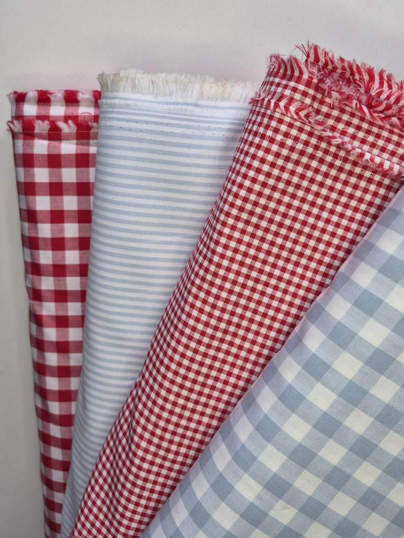 May include: Four rolls of fabric in various patterns. The fabrics include red and white gingham, light blue and white stripes, and red and white gingham. The edges of the fabric are frayed.