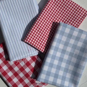 May include: Four folded fabric swatches in various patterns. There is a light blue and white striped fabric, two red and white gingham fabrics, and a light blue and white gingham fabric. The fabrics are arranged on a white surface.
