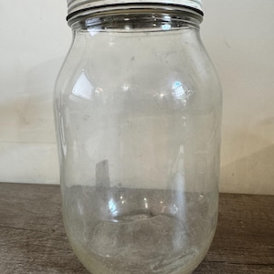 Peut inclure: Un bocal en verre transparent avec une large ouverture et un couvercle en métal. Le bocal est cylindrique avec une base arrondie. Le couvercle est argenté avec un bord blanc. Le bocal semble être vintage ou antique.