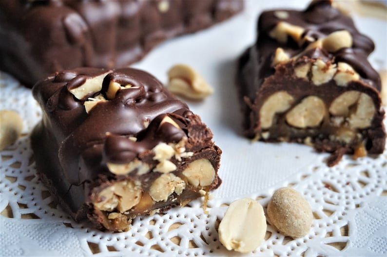 May include: Close-up of chocolate peanut butter bars with peanuts and caramel. The bars are on a white doily.