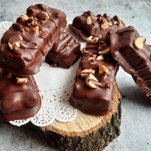 May include: A close-up of several chocolate peanut butter bars with peanuts on top. The bars are arranged on a wooden slice with a white doily.