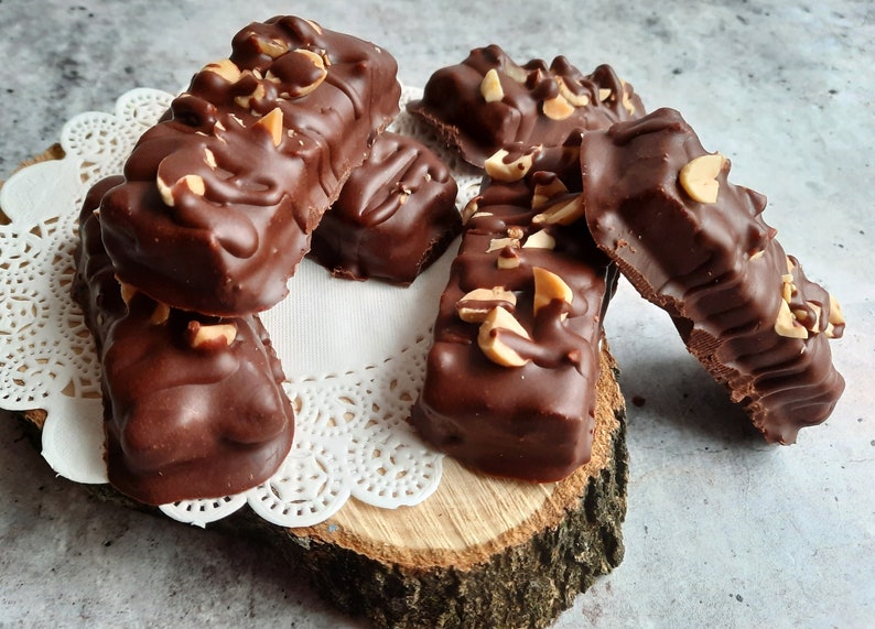 May include: A close-up of several chocolate peanut butter bars with peanuts on top. The bars are arranged on a wooden slice with a white doily.