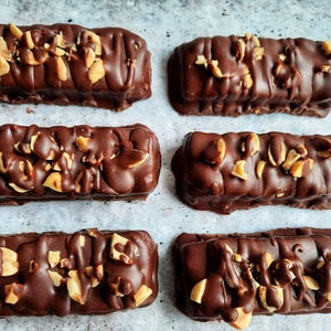 May include: Six chocolate peanut butter bars with chopped peanuts on top, arranged in two rows of three on a white surface.