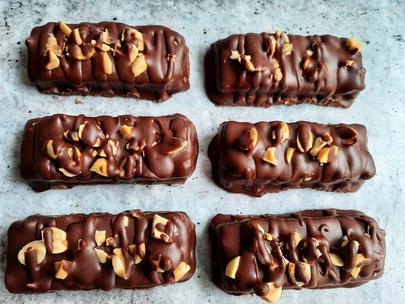 May include: Six chocolate peanut butter bars with chopped peanuts on top, arranged in two rows of three on a white surface.