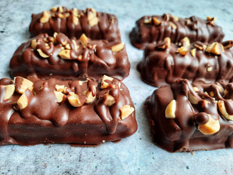 May include: Six chocolate peanut butter bars with chopped peanuts on top. The bars are arranged in two rows of three on a light blue surface.