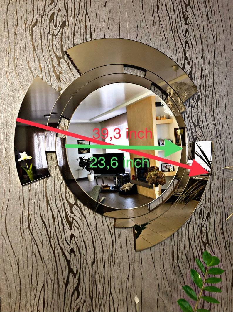 K&ouml;nnte beinhalten: Ein gro&szlig;er, runder, goldfarbener Spiegel mit geometrischem Design. Der Spiegel ist 39,3 Zoll breit und 23,6 Zoll hoch.