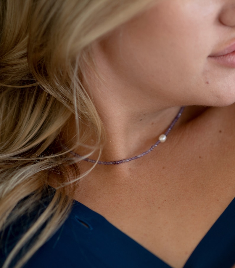 May include: A dainty necklace featuring tiny purple beads and a solitary white pearl pendant.