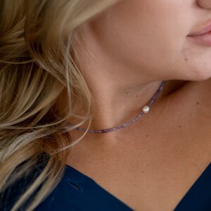 May include: A dainty necklace featuring tiny purple beads and a solitary white pearl pendant.