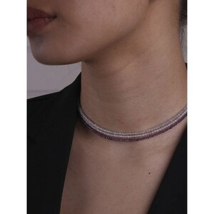 May include: A layered choker necklace with three strands of small, round beads. The top strand is white, the middle strand is light purple, and the bottom strand is a darker shade of purple.