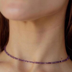 May include: A delicate purple gemstone choker necklace. The necklace is made of small, round beads and is worn close to the neck.