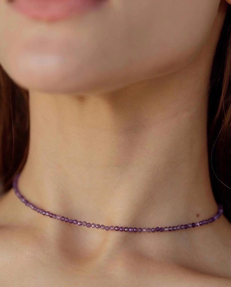 May include: A delicate purple gemstone choker necklace. The necklace is made of small, round beads and is worn close to the neck.