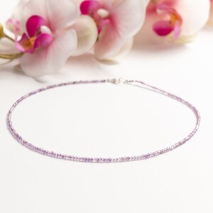 May include: A delicate necklace made with small, light purple amethyst beads. The necklace is on a white background with pink orchid flowers.