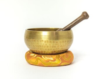 May include: A gold singing bowl with a wooden striker, resting on a patterned orange cushion.