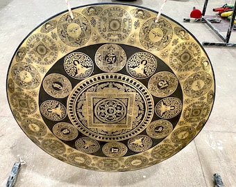 May include: A large, round, gold-colored gong with intricate black and gold designs. The gong has a central mandala with smaller mandalas surrounding it.