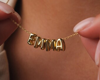 May include: A gold necklace with the name "EMMA" spelled out in individual letters.