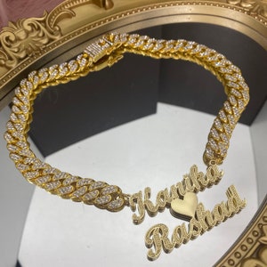 Peut inclure: Collier chaîne en or avec un pendentif en forme de cœur et deux noms, "Karika" et "Rashaad", écrits en cursive.