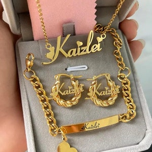 May include: Gold jewelry set with the name "Kaizlei" on a necklace, earrings, and bracelet. The set is displayed in a gray velvet box.