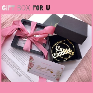 May include: A gift box with a pink ribbon, containing jewelry. Inside, a necklace and gold hoop earrings with the name "Camille" are visible. A thank you card with floral accents is also present. The text "GIFT BOX FOR U" is at the top.