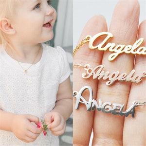 Może przedstawiać: Trzy złote naszyjniki z imieniem "Angela" napisanym w r&oacute;żnych stylach. Naszyjniki znajdują się na dłoni, przy czym g&oacute;rny naszyjnik jest złoty, środkowy r&oacute;żowo-złoty, a dolny srebrny.
