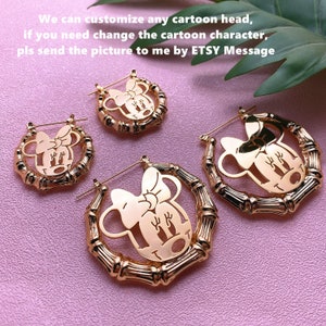 May include: Three pairs of gold-toned hoop earrings with a cutout design of a cartoon character with a bow. The character is similar to Minnie Mouse. The earrings are made of a bamboo-like material.