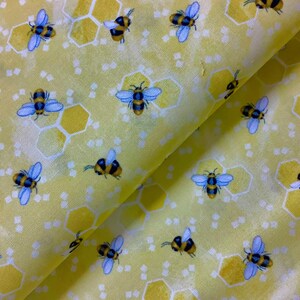 May include: Yellow fabric with a repeating pattern of honeycombs and cartoon bees. The bees are yellow and black with blue wings.