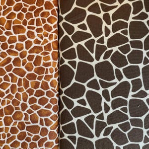 May include: Two fabric samples with giraffe print patterns. One features a brown and white pattern, while the other has a tan and white design. The fabric is folded, showcasing the repeating animal print.