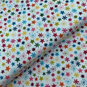 May include: White fabric featuring a repeating pattern of colourful stars and starbursts in shades of red, orange, yellow, green, blue, and pink. The fabric is likely cotton or a similar material.