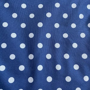 May include: A fabric textile featuring a repeating pattern of solid white polka dots evenly spaced across a deep blue background. The material displays a visible woven texture with subtle folds and creases throughout the surface of the cloth.
