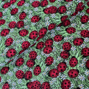 May include: Fabric featuring a repeating pattern of red ladybirds with black spots, set against a green backdrop with white daisy flowers and blades of grass.