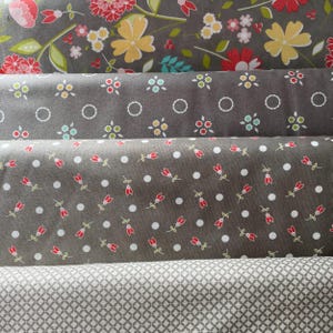 May include: Four rolls of fabric with diverse floral and geometric designs. The top roll displays large flowers in red, yellow, and pink on a grey backdrop. The other rolls have smaller floral and dot patterns in red, white, and grey.