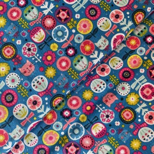 May include: A close-up of blue fabric featuring a repeating pattern of colourful floral and cat face designs. The pattern includes pink, yellow, and white flowers, along with dragonfly and leaf motifs. The fabric is folded diagonally.