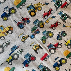 May include: A textile featuring a repeating pattern of tractors in various colours, including blue, yellow, green, and red. The tractors are depicted with large wheels and detailed features, set against a light grey background.