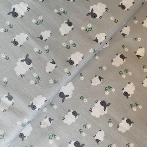 May include: Grey fabric featuring a repeating pattern of white sheep with black faces and ears, and small white flowers with green leaves. The fabric is folded, showing the pattern at different angles.