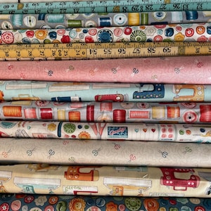 May include: A selection of fabric rolls with sewing-related patterns. Designs include spools of thread, buttons, scissors, and sewing machines in various colours. Some rolls feature measuring tape patterns. The fabrics are stacked, showcasing a variety of colours and designs.