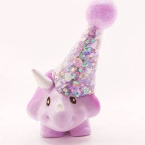 May include: A purple dinosaur figurine wearing a sparkly purple party hat with a fuzzy pom-pom on top.