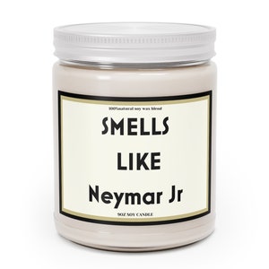 Może przedstawiać: Beżowa świeca z wosku sojowego w szklanym słoiku z białą pokrywką. Na etykiecie widnieje napis "Smells Like Neymar Jr" pogrubioną czcionką. Świeca ma 255g.