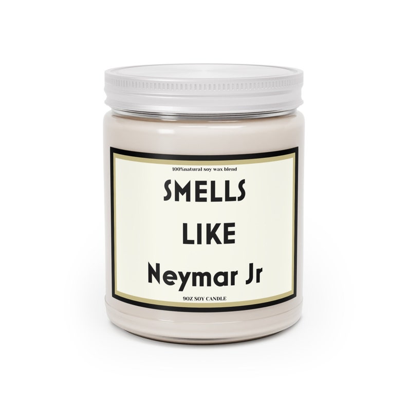 Może przedstawiać: Beżowa świeca z wosku sojowego w szklanym słoiku z białą pokrywką. Na etykiecie widnieje napis "Smells Like Neymar Jr" pogrubioną czcionką. Świeca ma 255g.