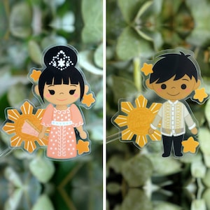 May include: Two transparent stickers featuring cartoon figures. One depicts a woman in a pink dress with a fan, the other a man in a traditional shirt. Both are set against a sunburst design with the text "Pinny Planet".