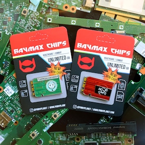 Pode incluir: Dois mini pinos Baymax Chips em cartões vermelhos e pretos. Um pino é verde com um rosto sorridente, o outro é vermelho com uma caveira. Os cartões dizem "Baymax Chips" e "Unlimited GB".