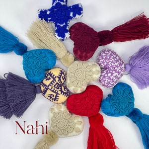 May include: Assortment of colorful embroidered heart-shaped ornaments with tassels. The hearts are in shades of blue, purple, red, and cream. The tassels are in matching colors. The word "Nahi" is written in red at the bottom of the image.