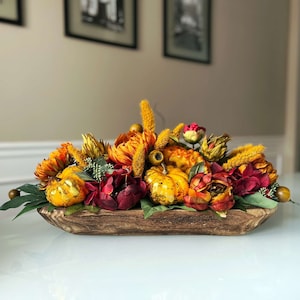 May include: A wooden bowl filled with a fall-themed centerpiece featuring faux gourds, pumpkins, and flowers in shades of orange, yellow, red, and green.