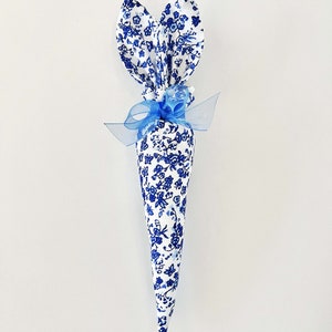 K&ouml;nnte beinhalten: Ein blauer und wei&szlig;er Osterhasen-Kegel aus Blumenstoff mit blauem Band und wei&szlig;en Perlenakzenten.