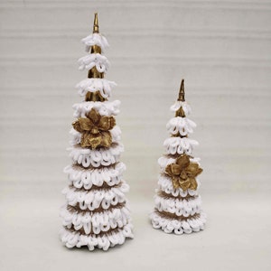 May include: Two white and gold Christmas trees made of burlap and fabric. The larger tree is taller than the smaller tree. Both trees have a gold flower accent.