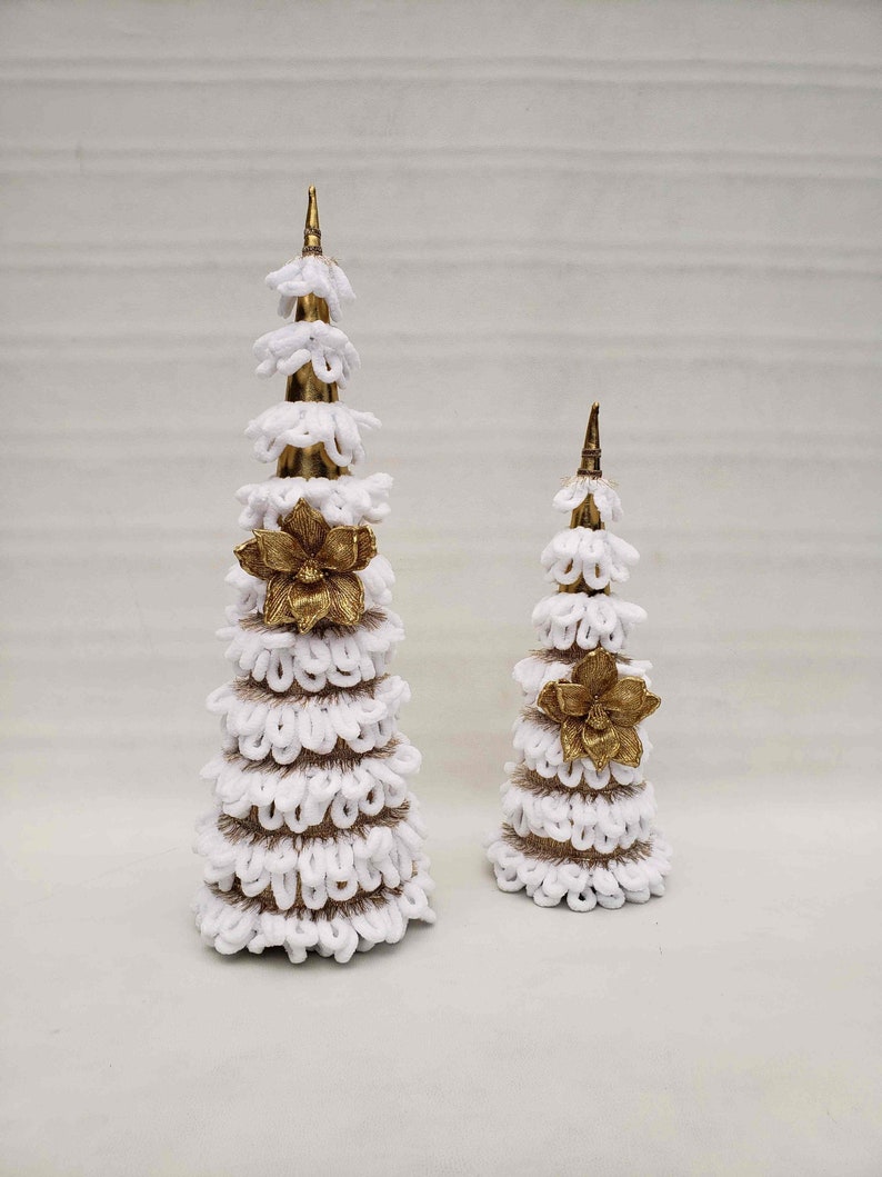May include: Two white and gold Christmas trees made of burlap and fabric. The larger tree is taller than the smaller tree. Both trees have a gold flower accent.