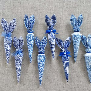 K&ouml;nnte beinhalten: Sieben blaue und wei&szlig;e Stoff-Karotten-Dekorationen mit Hasenohren. Die Karotten sind mit einem blauen und wei&szlig;en Blumenmuster verziert und haben blaue Schleifen.