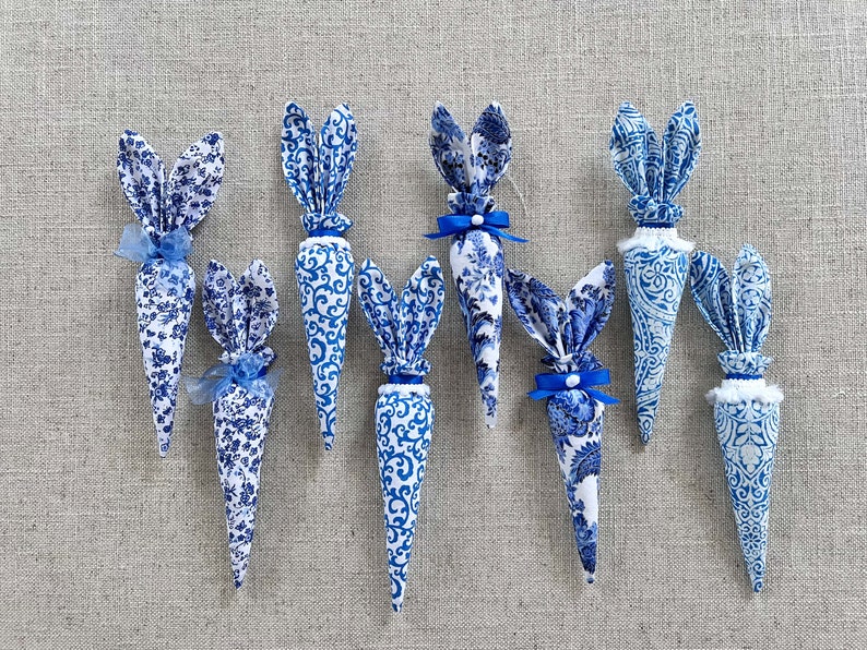 K&ouml;nnte beinhalten: Sieben blaue und wei&szlig;e Stoff-Karotten-Dekorationen mit Hasenohren. Die Karotten sind mit einem blauen und wei&szlig;en Blumenmuster verziert und haben blaue Schleifen.