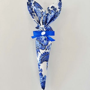 Peut inclure: Un c&ocirc;ne de lapin de P&acirc;ques en tissu bleu et blanc avec un ruban bleu et un bouton blanc.