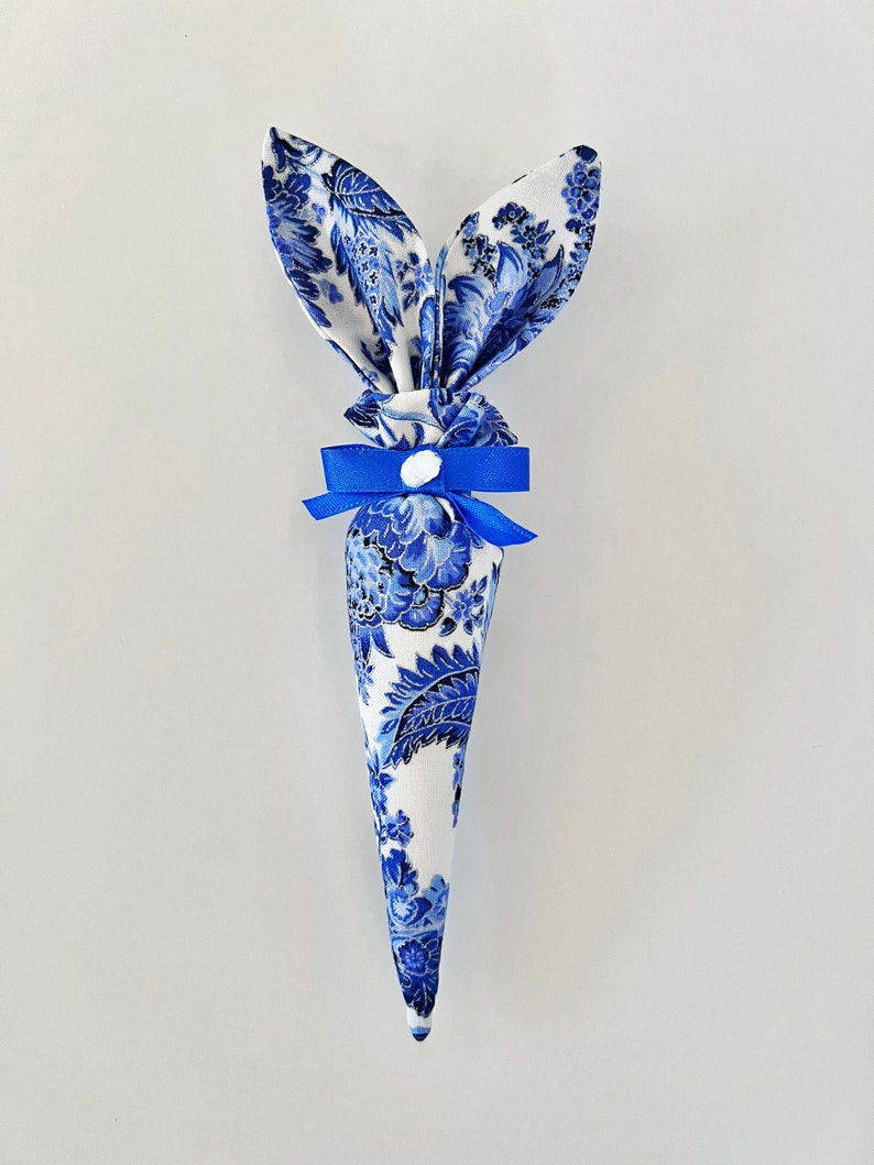 Peut inclure: Un c&ocirc;ne de lapin de P&acirc;ques en tissu bleu et blanc avec un ruban bleu et un bouton blanc.